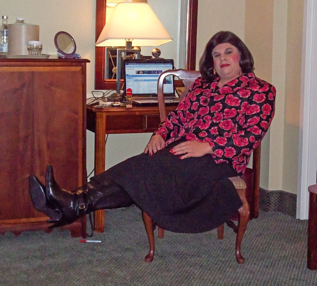 Person sitting on a chair with one leg crossed over the other, wearing a floral top and black skirt, in a well-furnished room with a lamp and desk in the background.